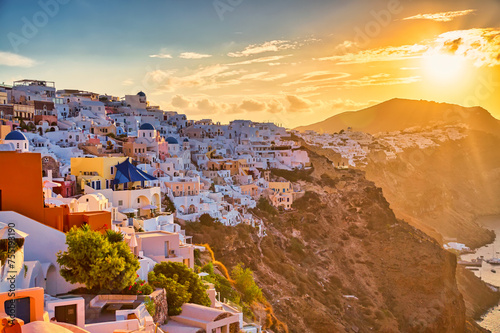 Aerial drone view of famous Oia village with white houses and blue dome churches during sunset on Santorini island, Aegean sea, Greece.