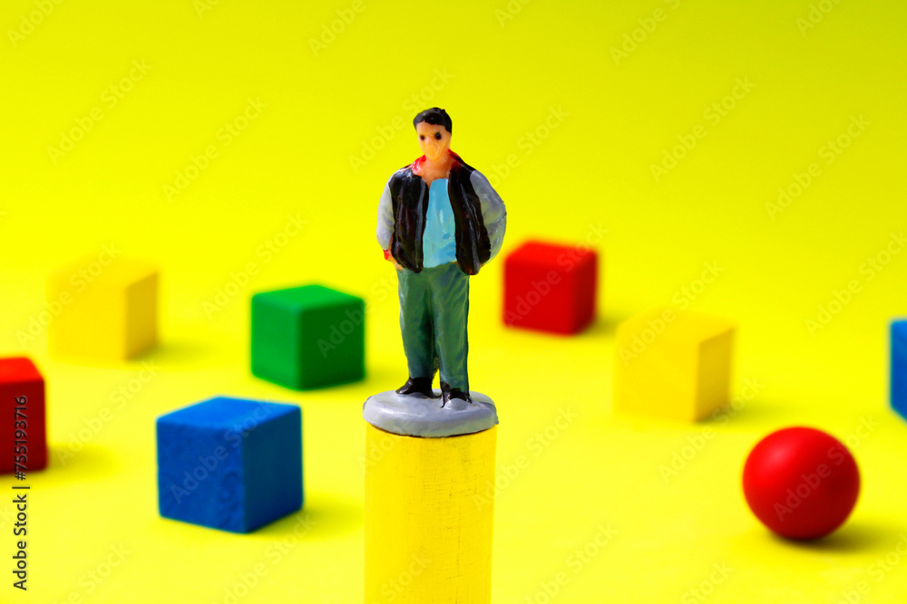 Man on cylinder at highest level surrounded by geometric figures of different colors Man on cylinder at highest level surrounded by geometric figures of different colors
