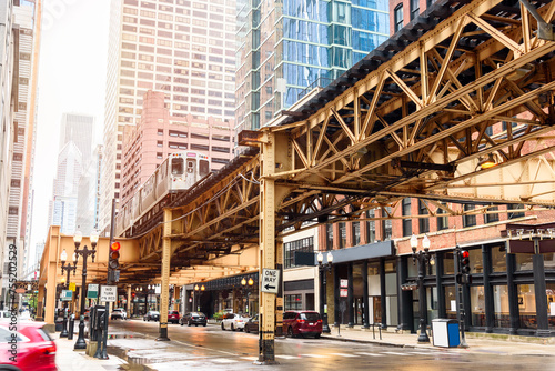 Low angle view of a train running on elevated tracks over a street lined with both modern high rises and traditional brick buildings in downtown Chicago photo