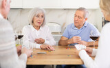 Senior men and women play card game poker during friendly gatherings at home. Couple enthusiastically participate in game, believe in luck, collect chips, distribute winnings