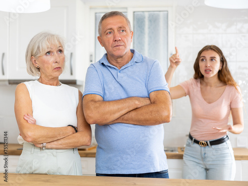 Adult daughter scolds elderly parents, mom and dad, in a modern kitchen