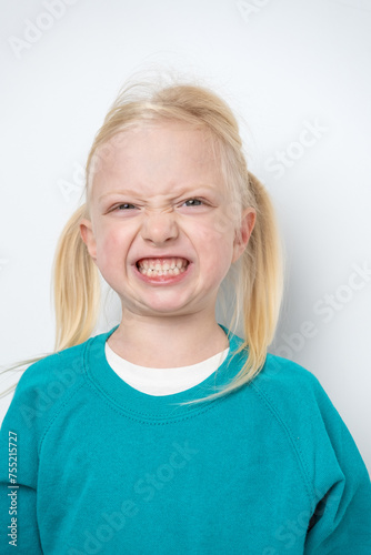 Close-up portrait of a little girl with blond hair smiling and showing teeth on a white background