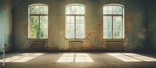 An empty room with three windows casting light over a radiator in the corner. The windows are closed, with curtains drawn. The radiator appears old and worn but functional.