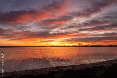 A magnificent sunrise with pink and orange tinted clouds and reflections on a calm lake with a shoreline in the foreground at Lake Broadwater near Dalby in Queensland, Australia. photo