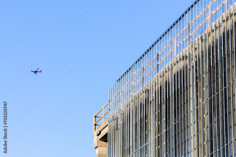 An airliner flying high and above a sheet-metal structure under construction An airliner flying high and above a sheet-metal structure under construction