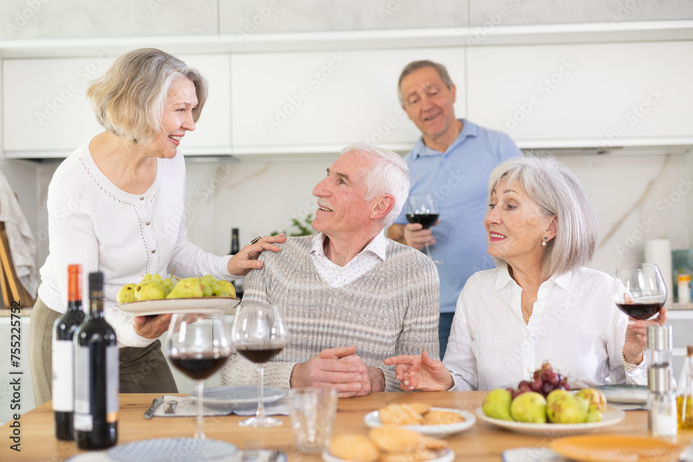Group of happy elderly people drink red wine and chat at festive table. High quality photo