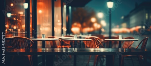 A table and chairs are arranged neatly outside a restaurant, with a blurred background of the restaurant cafe at night. The setting suggests a welcoming and cozy atmosphere for diners. photo