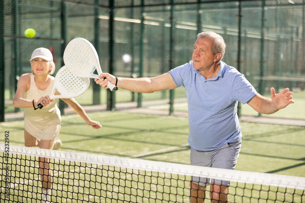 Fototapeta premium Dynamic old man and woman playing Padel Tennis with partners in the open air tennis court