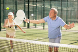 Dynamic old man and woman playing Padel Tennis with partners in the open air tennis court