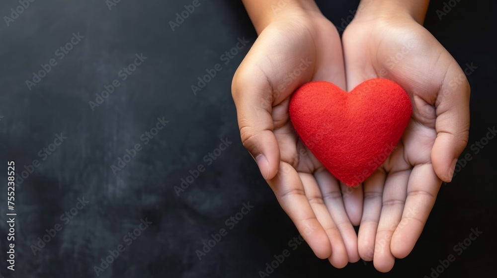 Red heart in the hands of a child on a black background.