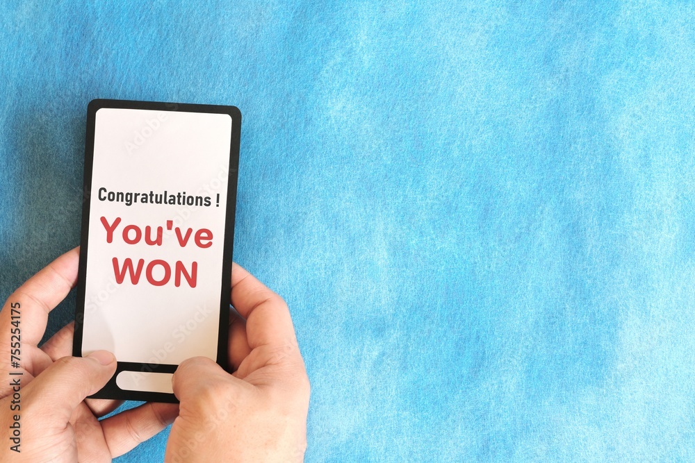 Winning text message scam concept. Hand holding mobile phone with congratulatory message in blue background.