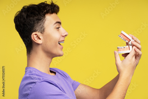 Smiling attractive young boy, teenager with braces holding orthodontic jaw, looking at her