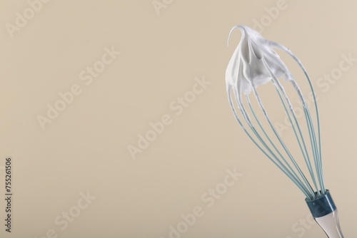 Whisk with whipped cream on beige background. Space for text
