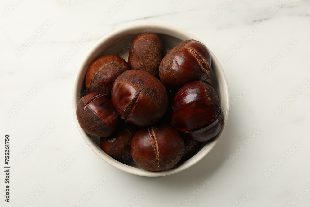 Roasted edible sweet chestnuts in bowl on white marble table, top view Roasted edible sweet chestnuts in bowl on white marble table, top view
