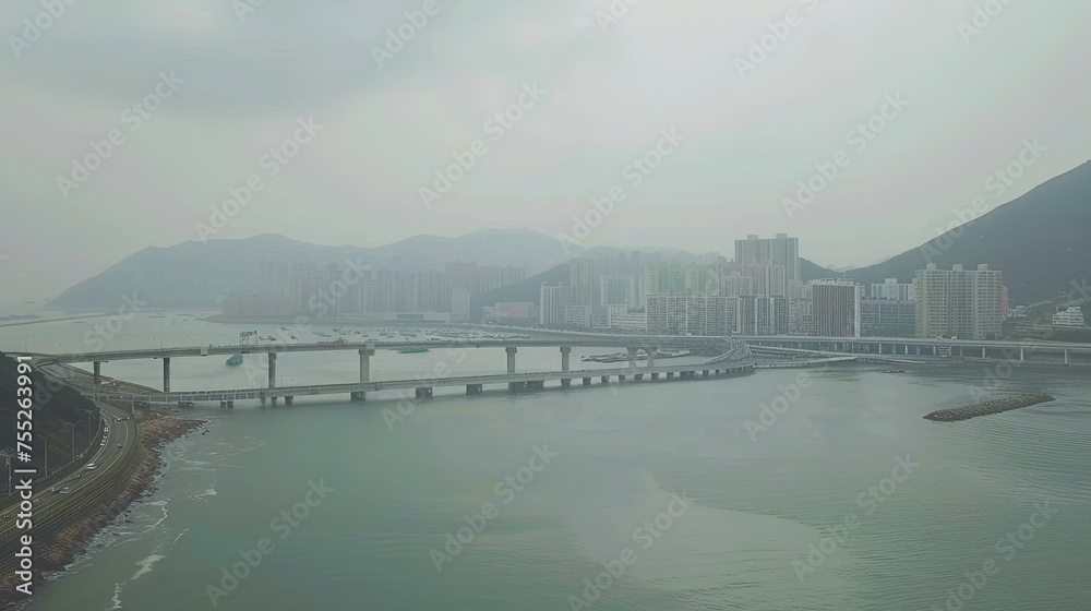 Aerial view of a curving bridge over water with urban skyscrapers against a backdrop of hazy mountains