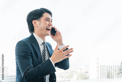 オフィスでスマホを使う若いアジア人ビジネスマン（営業トーク・電話・営業・アポ・営業活動）
