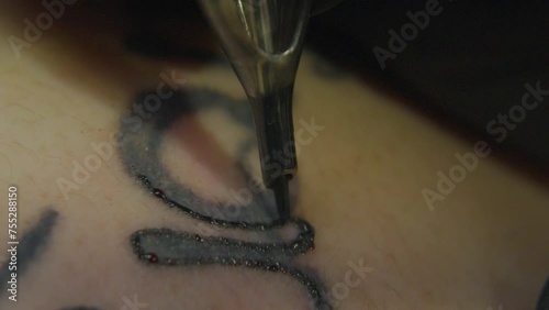 a fast moving tattoo needle inks the outline of an existing artwork causing droplets of blood to form on the surface of the skin photo