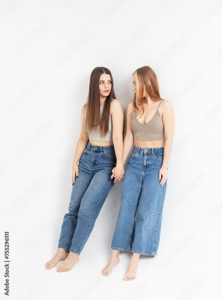 two smiling young women friends wearing jeans and tops isolated over white grey background two smiling young women friends wearing jeans and tops isolated over white grey background