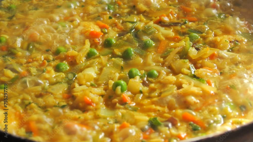 A large pan of bubbling risotto is boiling. Risotto with vegetables and pieces of chicken is prepared in the home kitchen close up A large pan of bubbling risotto is boiling. Risotto with vegetables and pieces of chicken is prepared in the home kitchen close up
