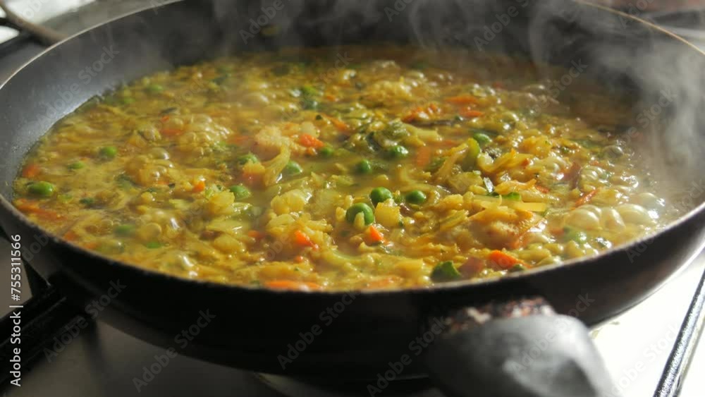 A large pan of bubbling risotto is boiling. Risotto with vegetables and pieces of chicken is prepared in the home kitchen A large pan of bubbling risotto is boiling. Risotto with vegetables and pieces of chicken is prepared in the home kitchen