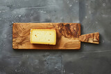 A slice of Limburger cheese rests atop a rectangular wooden cutting board, awaiting its role as a delectable ingredient in a savory dish.





