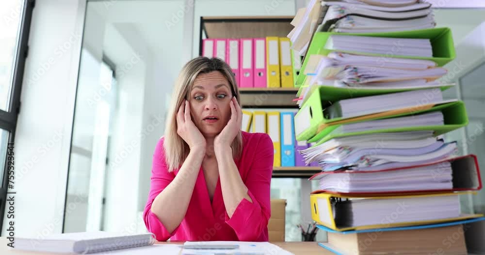 Woman clutches head looking at enormous stack of folders