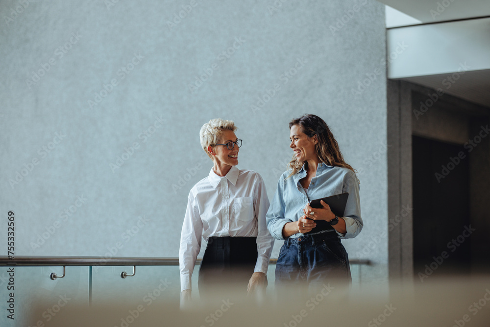 © Jacob Lund - Two business women having a discussion as they walk together in a modern office © Jacob Lund - Two business women having a discussion as they walk together in a modern office
