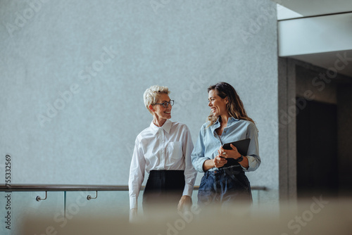 Two business women having a discussion as they walk together in a modern office photo