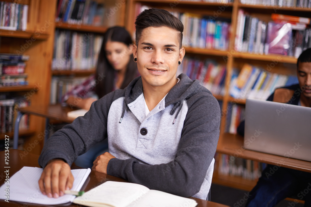 Young man, portrait or studying in library for test or scholarship on campus for class assignment. University student, face or happy for education or research in books for exam preparation by desk Young man, portrait or studying in library for test or scholarship on campus for class assignment. University student, face or happy for education or research in books for exam preparation by desk
