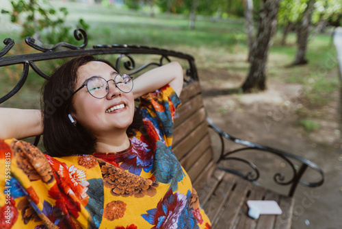 Relaxed and happy, an Asian woman enjoys her time alone on a park bench Woman in a vibrant floral shirt takes a break outdoors, smiling contentedl