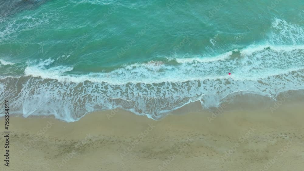 Top-down aerial view of a beach showing the foamy waves breaking along the sandy shore, creating a natural pattern contrast between the ocean and land. Top-down aerial view of a beach showing the foamy waves breaking along the sandy shore, creating a natural pattern contrast between the ocean and land.