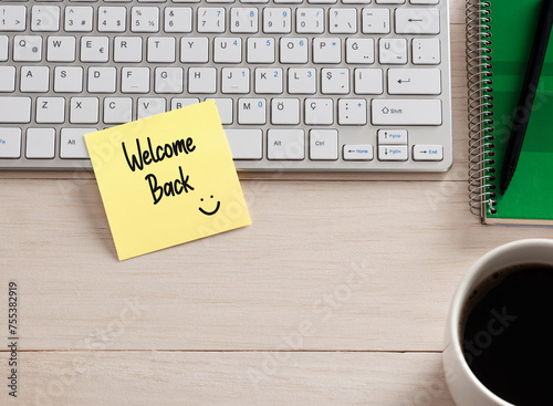 Welcome back message handwritten on a sticky note paper on the office desk. photo