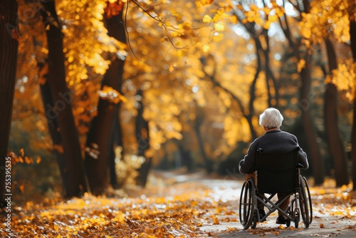 An elderly woman rides in a wheelchair in a fall park. A lonely old disabled female on a street strewn with yellow leaves.