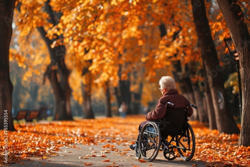 An elderly woman rides in a wheelchair in a fall park. A lonely old disabled female on a street strewn with yellow leaves.