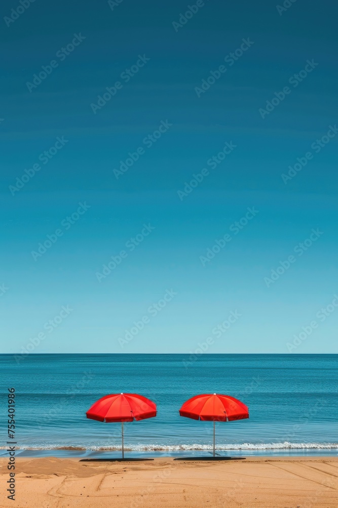 Two red beach umbrellas by the sea on a clear day.