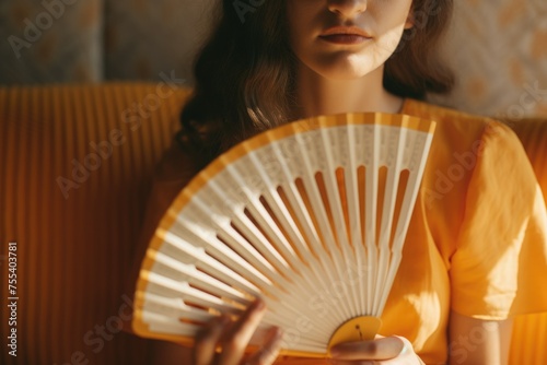 A woman sitting on a couch holding a fan. Suitable for lifestyle and home comfort concepts