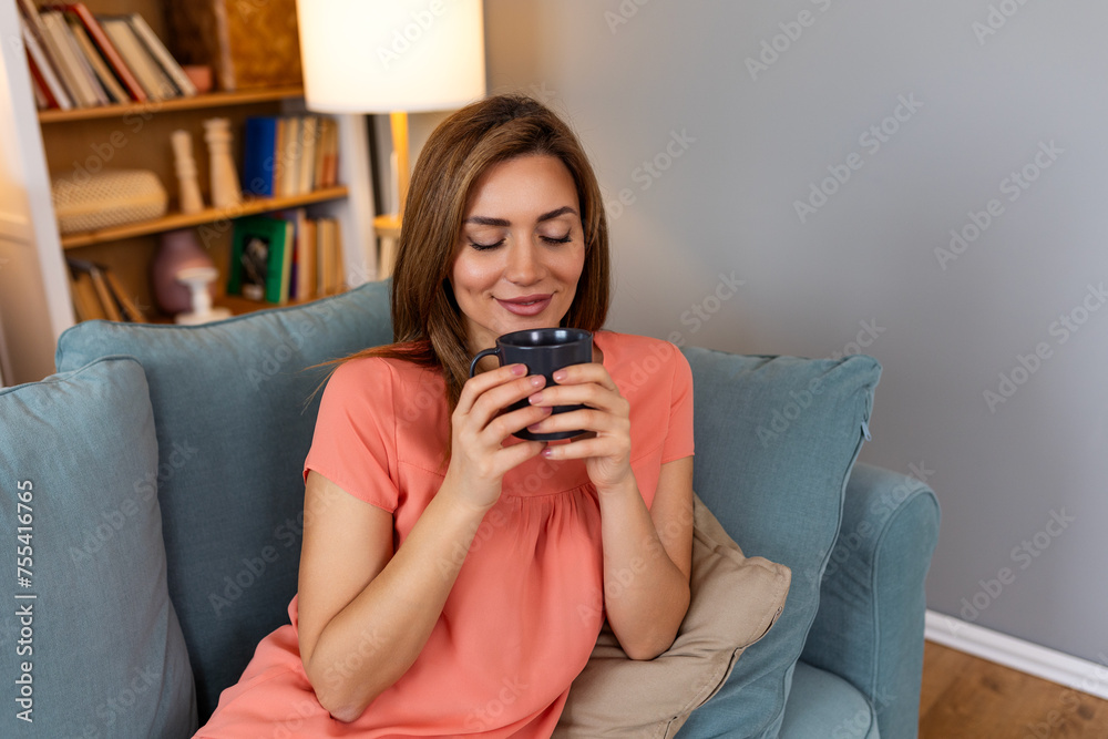 Young happy relaxed Latin woman enjoying quiet moments at home with cup of tea or coffee, smiling female holding mug with hot drink resting on sofa in living room and dreaming, relaxing of everything Young happy relaxed Latin woman enjoying quiet moments at home with cup of tea or coffee, smiling female holding mug with hot drink resting on sofa in living room and dreaming, relaxing of everything