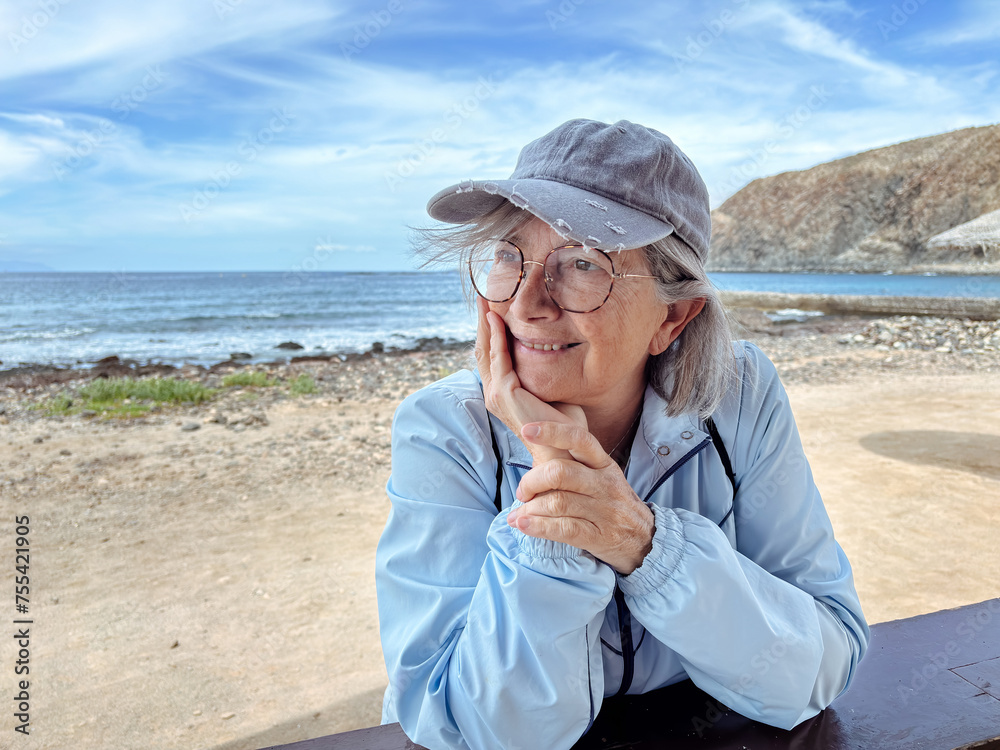 Attractive senior gray-haired woman at the beach looking away enjoys freedom and retirement, horizon over water on background