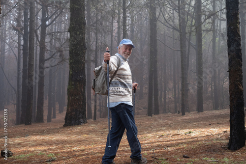 Active happy senior retired man with backpack walking in mountain forest on a foggy day with the help of poles enjoying nature, freedom and free time. Forest background with bare trees © luciano