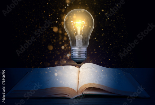 Glowing light bulb over a textbook on a dark background with glitter.  Concept to produce new idea based on knowledge.