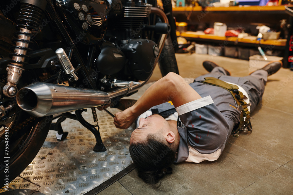 Garage worker fixing bottom part of motorcycle