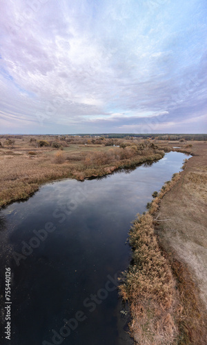 Aerial vertical panorama of blue river flowing in autumn valley with scenic cloudy sky