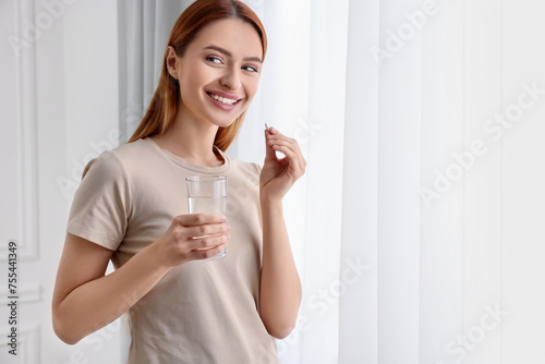 Beautiful young woman taking vitamin pill at home. Space for text