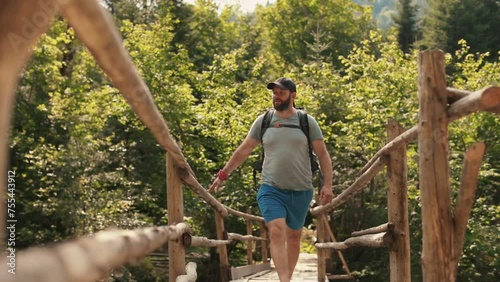 A man in hiking gear with a backpack walks across an epic suspension bridge in a national park. A cinematic adventure of traveling in the mountains. A man walks through a small town on a mountain rive photo