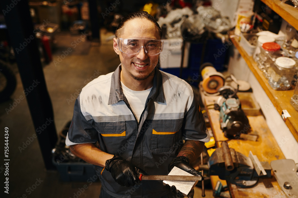 Portrait of smiling mechanic in goggles holding raspfile