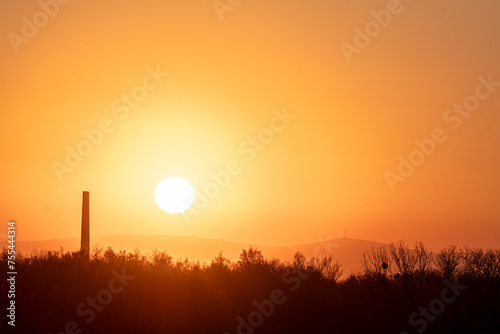 Yellow sunset in the landscape. Chimney in the foreground. Mountains in the background