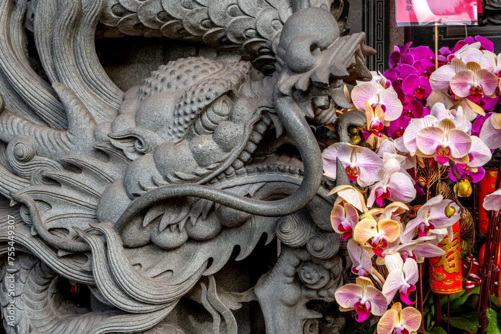 Fototapeta premium Ornate gray figurine with colorful orchids at the Songshan Ciyou Buddhist Temple in Taipei