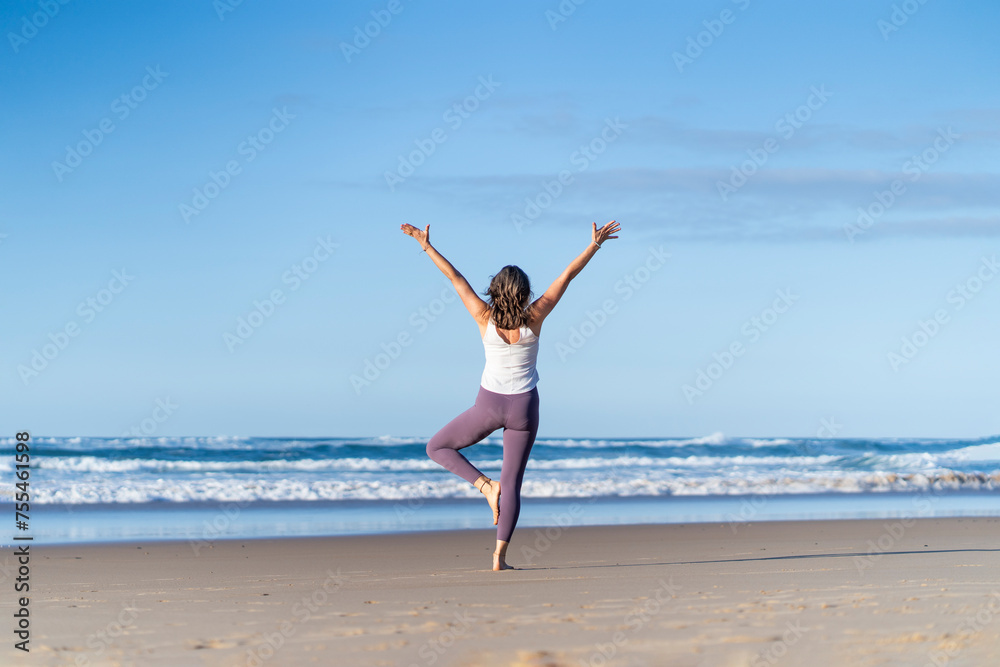 Woman doing tree yoga pose with arms raised at beach Woman doing tree yoga pose with arms raised at beach