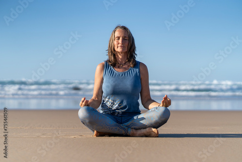 Mature woman sitting in lotus position on sand at beach photo