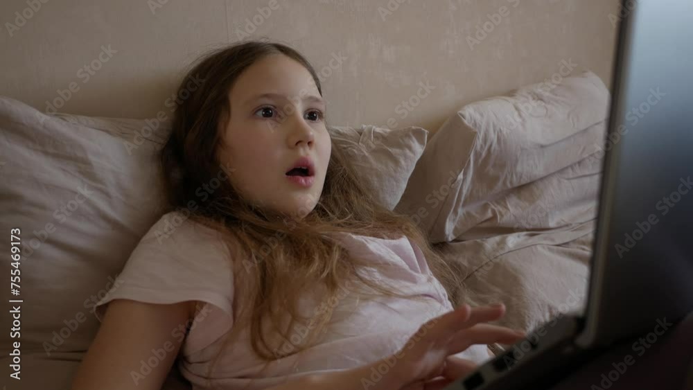 Surprised face of a teenage girl, wow, gesture for information or news. Schoolgirl lying on bed and using laptop in bed. Online communication on social networks, winning in chat Surprised face of a teenage girl, wow, gesture for information or news. Schoolgirl lying on bed and using laptop in bed. Online communication on social networks, winning in chat